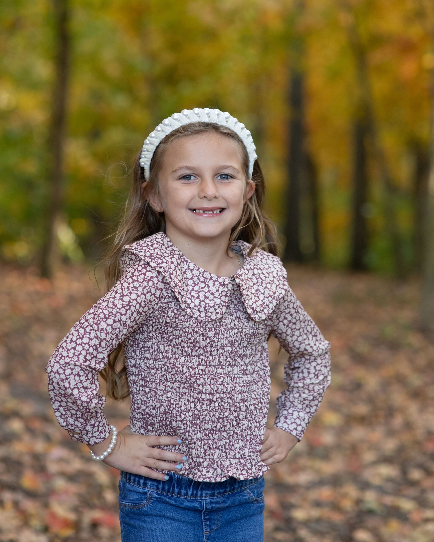 Portrait of youth wearing floral print top and white headband against autumn leaves.