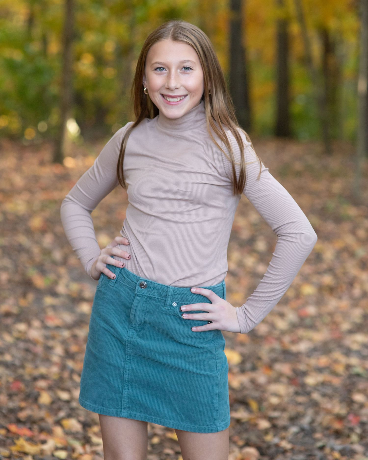 Portrait of person in beige turtleneck and teal skirt against fall foliage.
