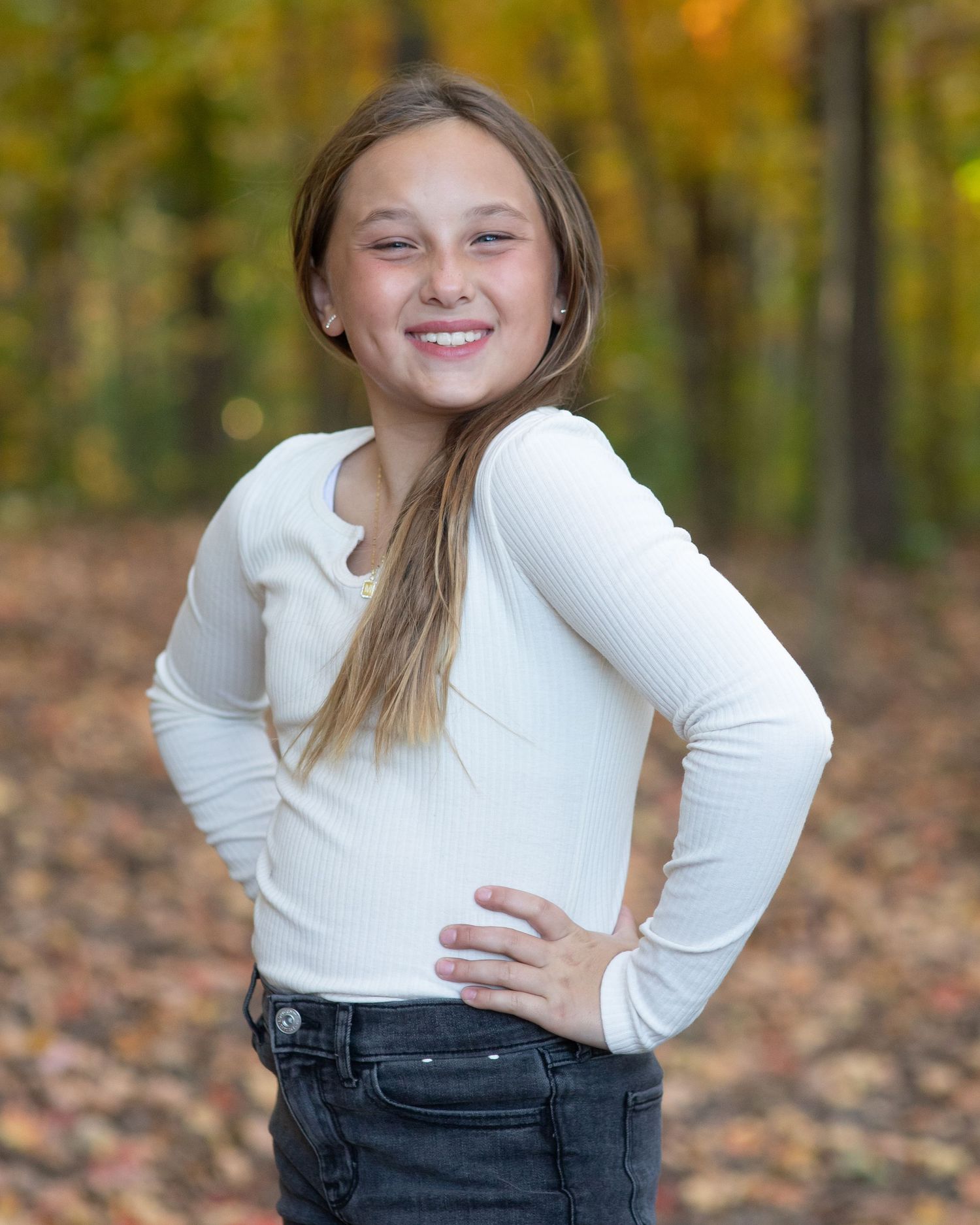 Portrait of person in white sweater and jeans posing against autumn forest background.