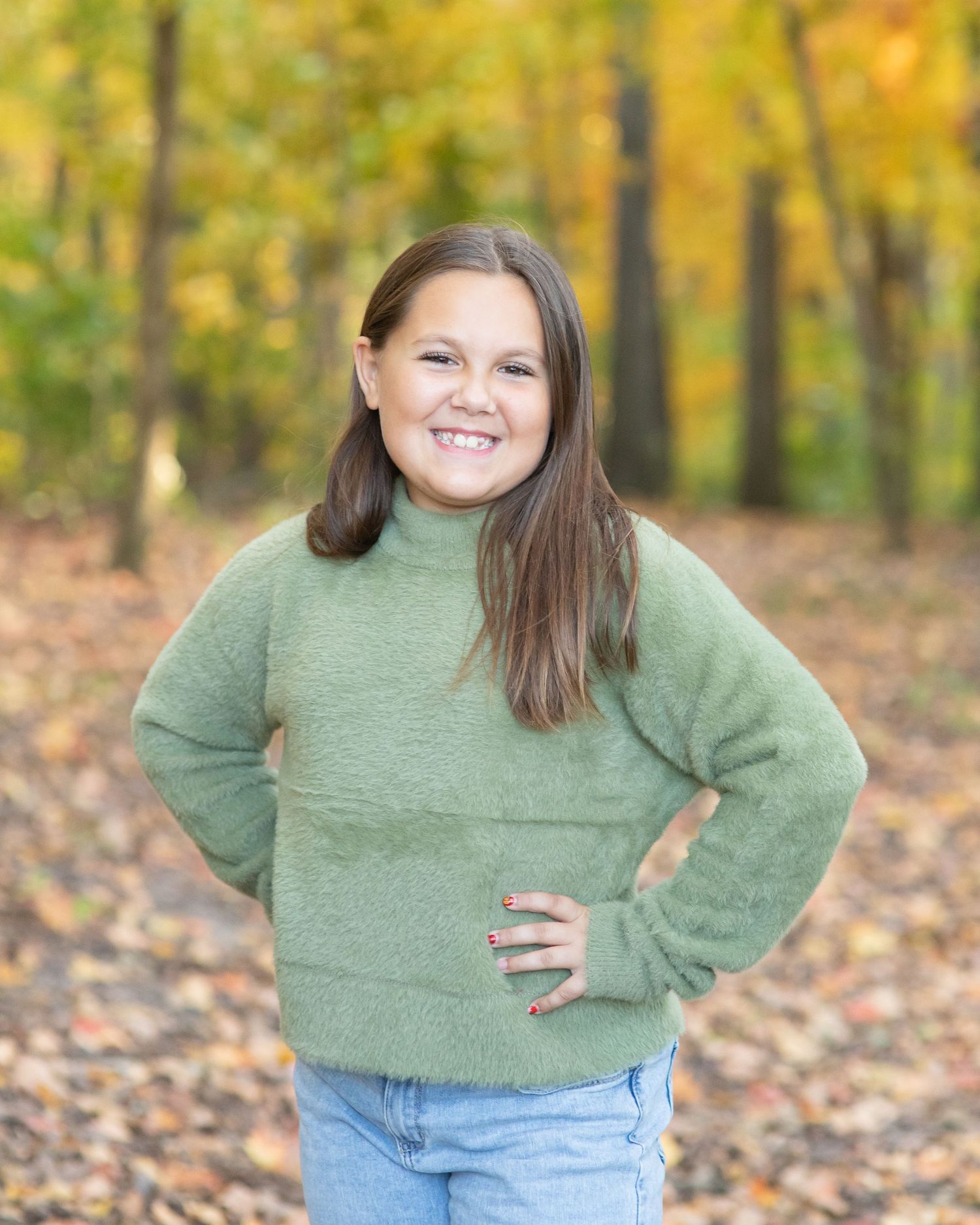 Portrait of person in green sweater and jeans with autumn leaves in background.