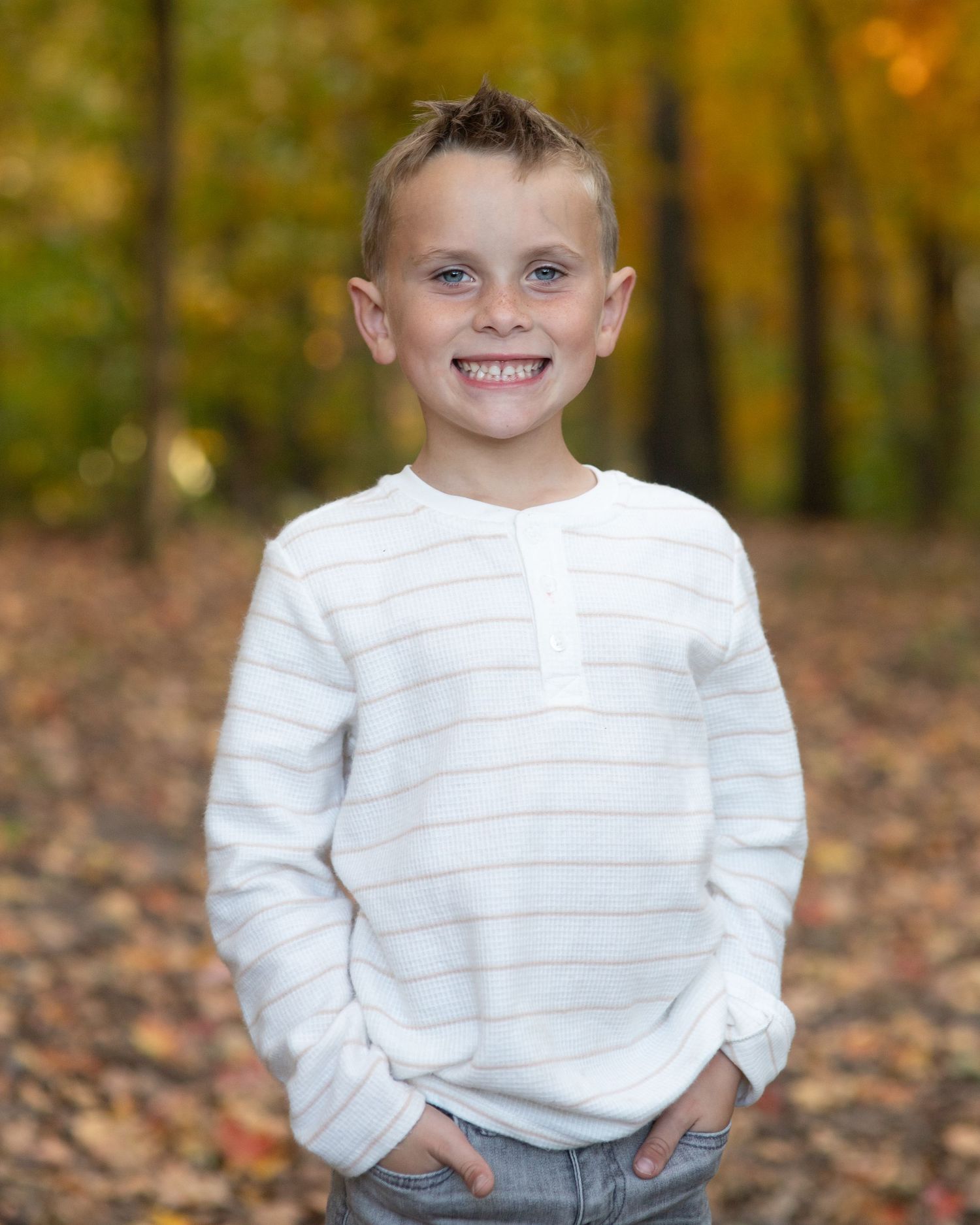 Portrait of youth in striped white henley shirt against fall foliage background.