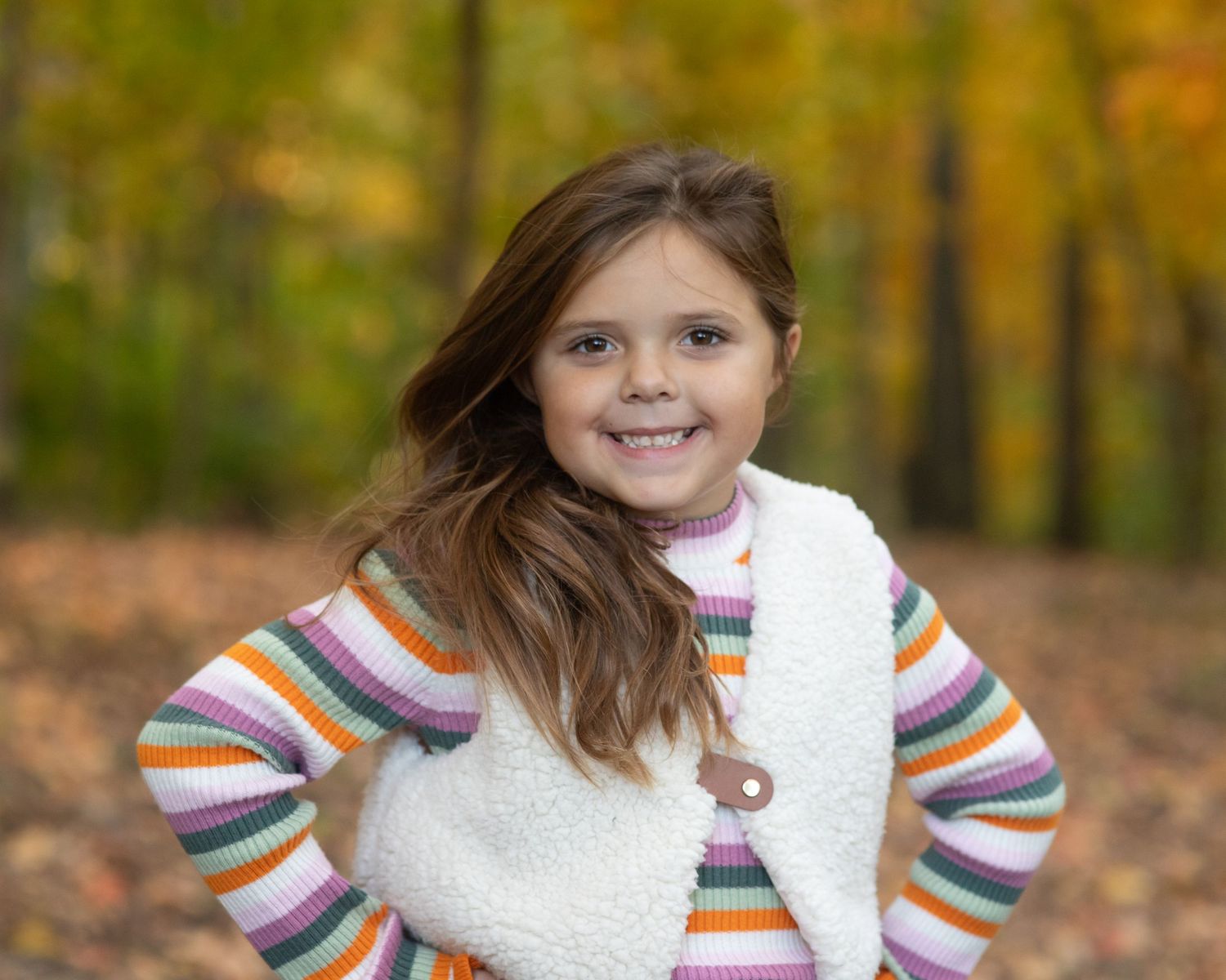 Child wearing a rainbow striped sweater poses during fall photo session.