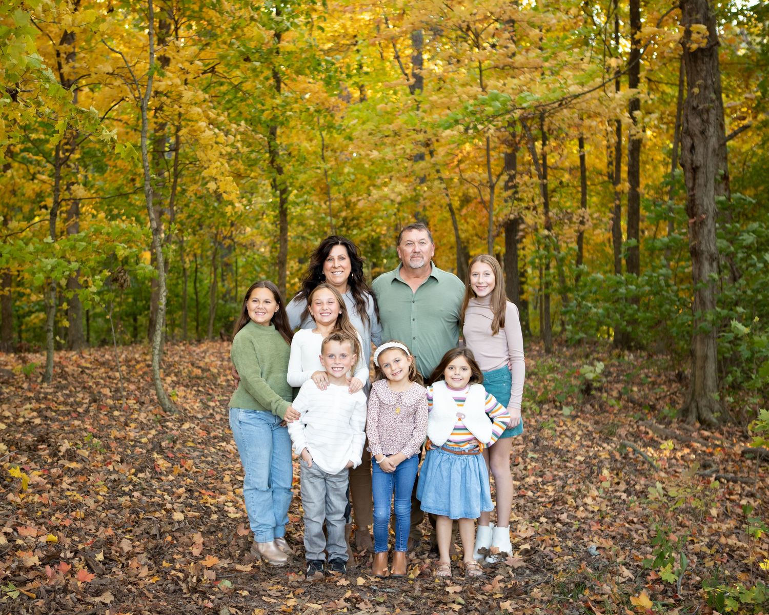 Family group portrait arranged on fallen leaves in an autumn woodland setting.