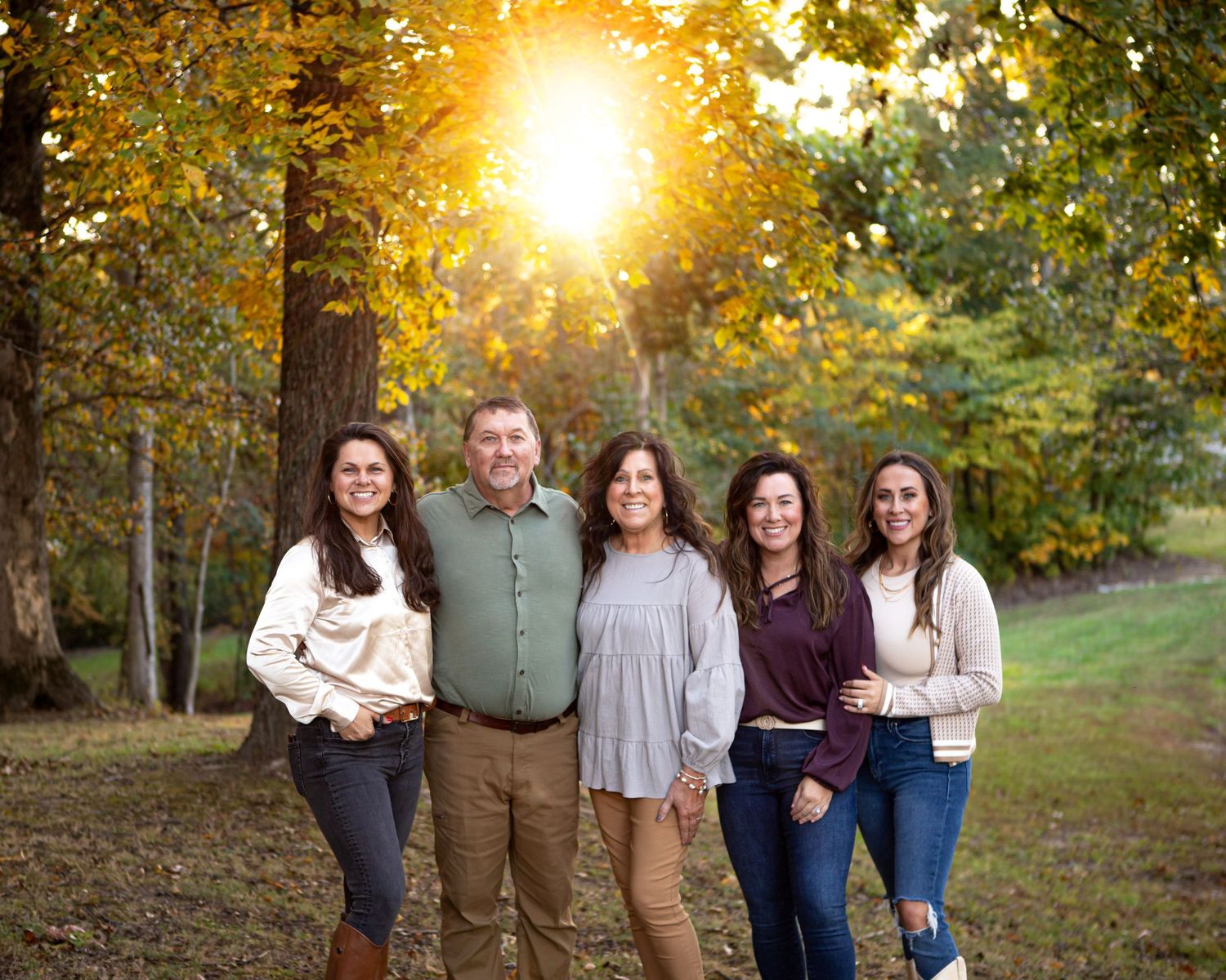 Family photo session at golden hour with sunburst through autumn trees.