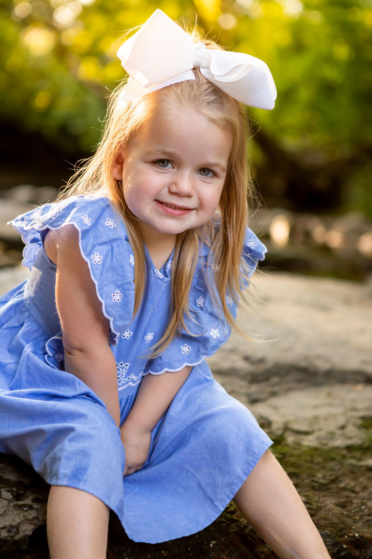Young child in blue ruffled dress poses on rocks during outdoor portrait session.