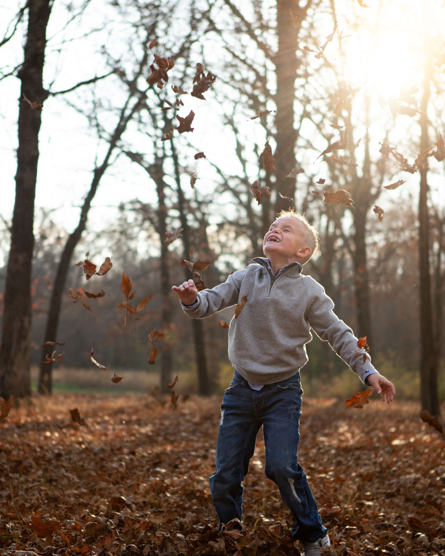 A child plays in fallen autumn leaves during golden hour in the woods.
