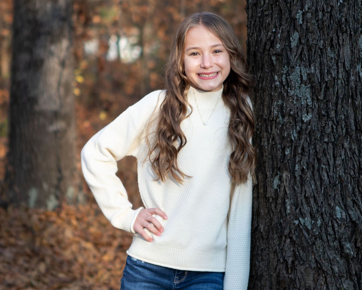 A portrait session against a dark tree trunk in an autumn forest setting.
