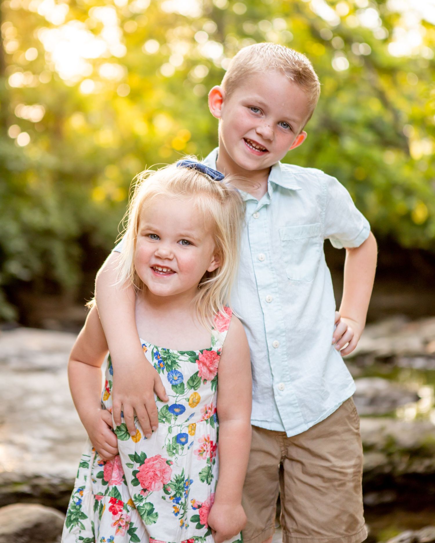 Children in summer outfits play together by a rocky creek.