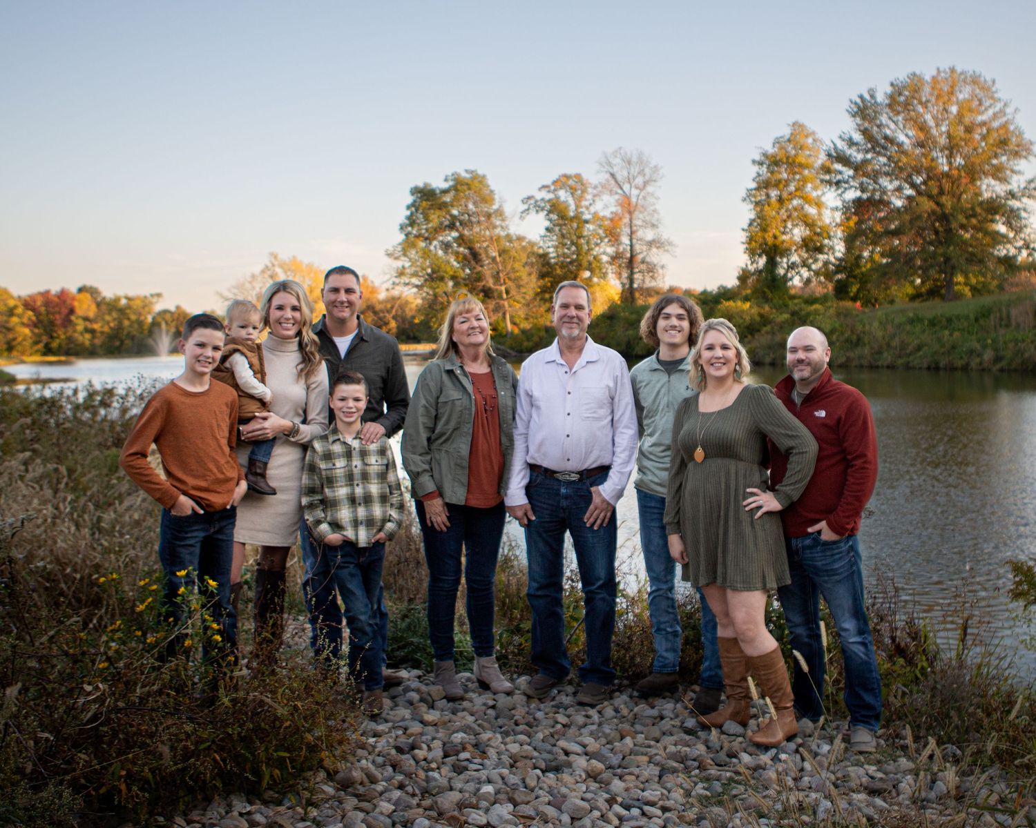 A group poses together on a rocky shoreline with autumn trees and water in the background.