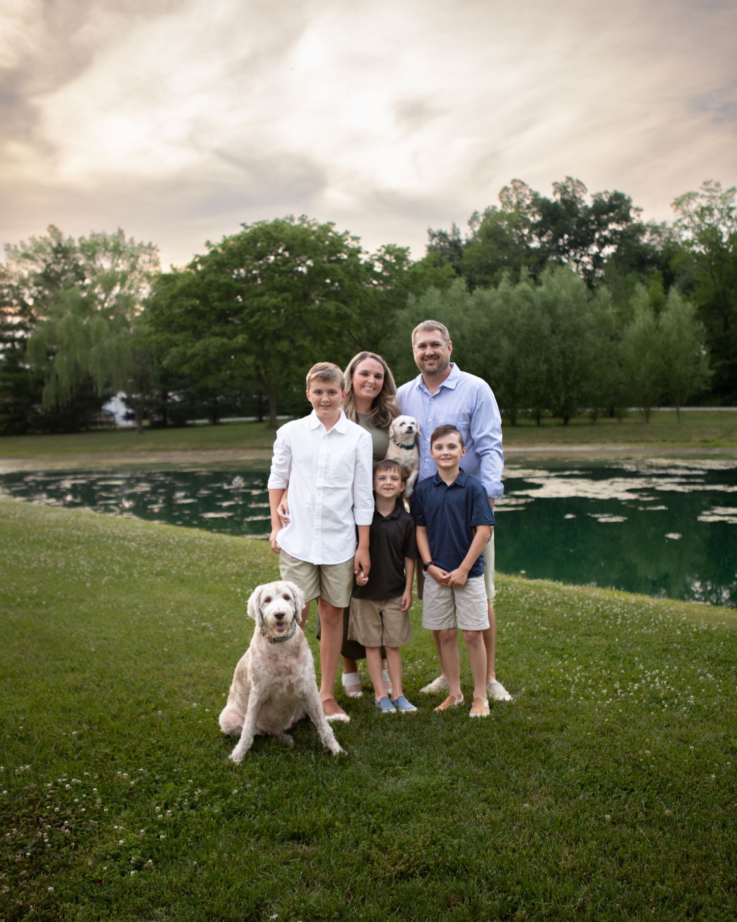 Family and their white dog pose together on grassy field during sunset photo session.