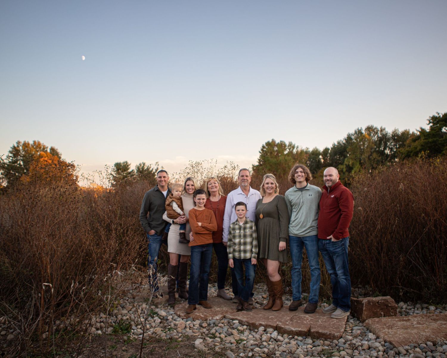 Extended family gathering for outdoor portraits at sunset against natural backdrop.