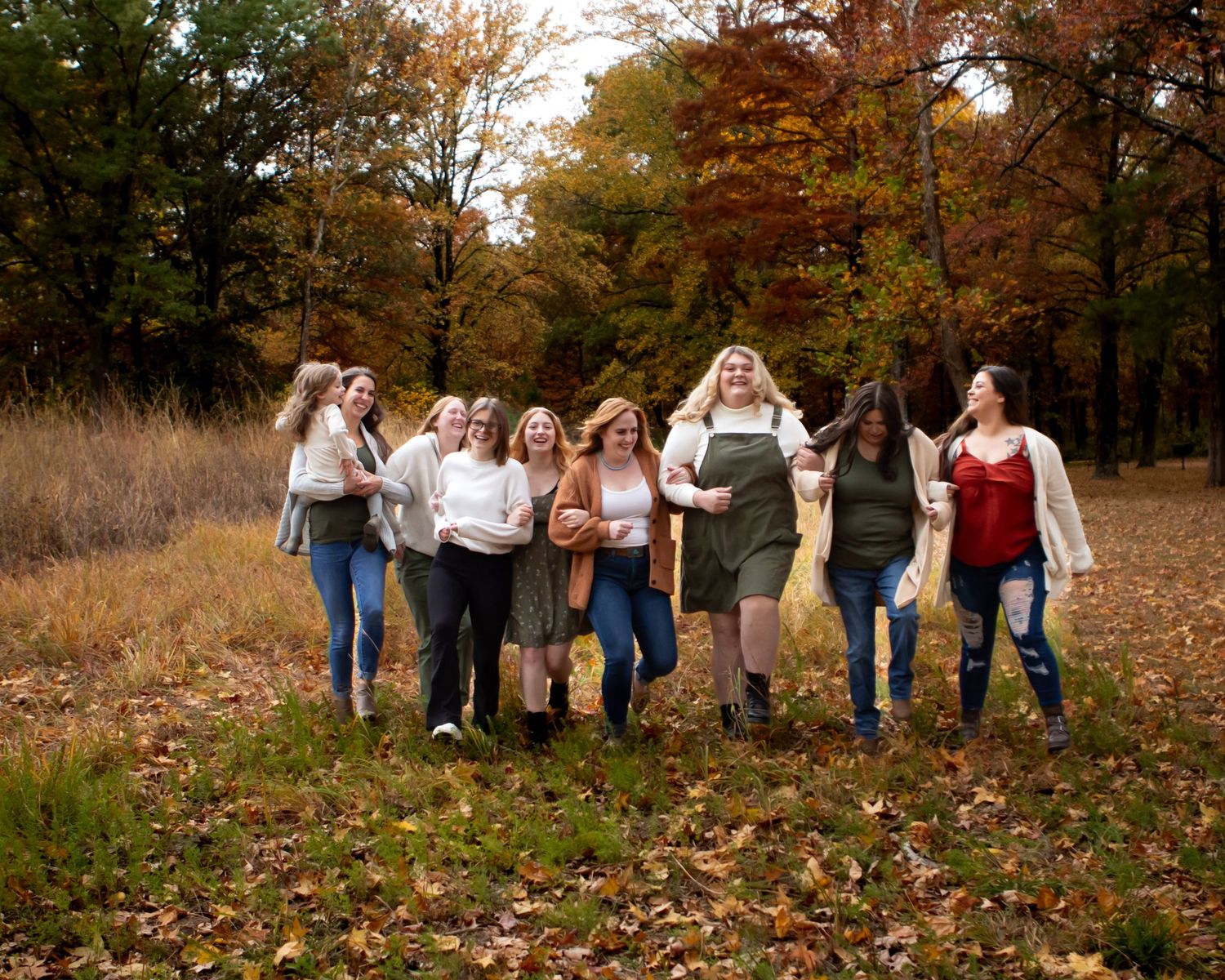 Friends posing together in casual attire against a backdrop of autumn trees and fallen leaves.