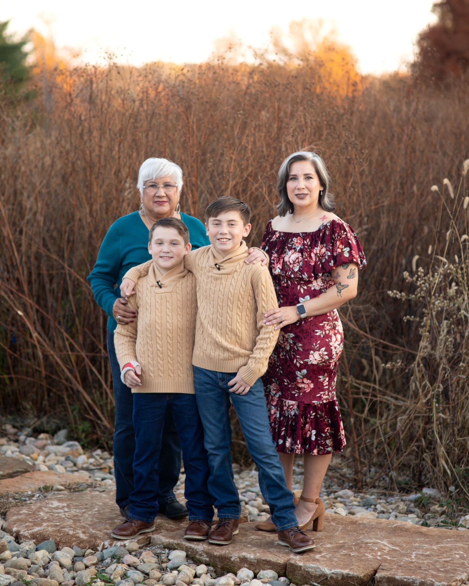 Three generations pose together on stone steps during golden hour in autumn.