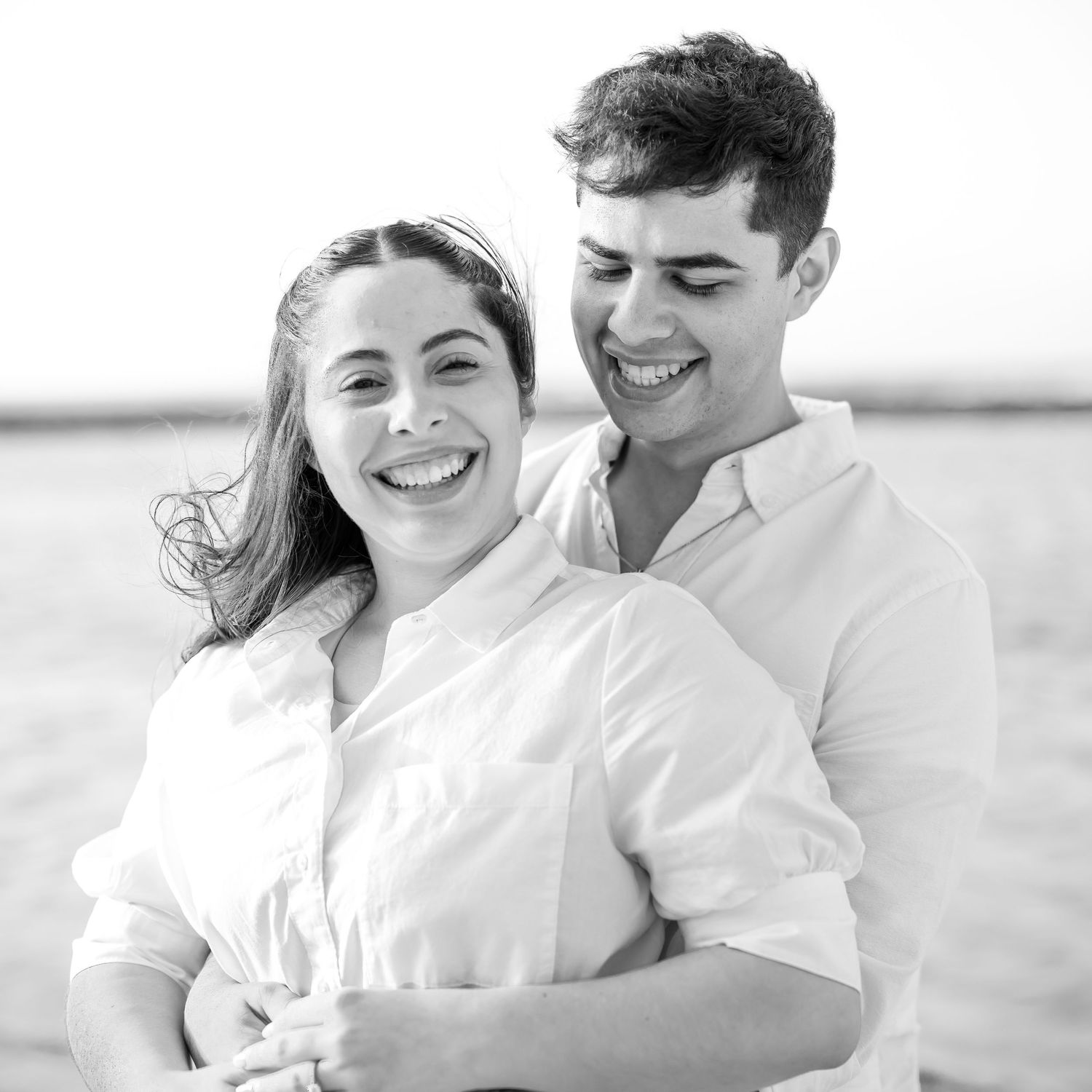 Black and white portrait of a laughing couple in white clothing embracing outdoors.