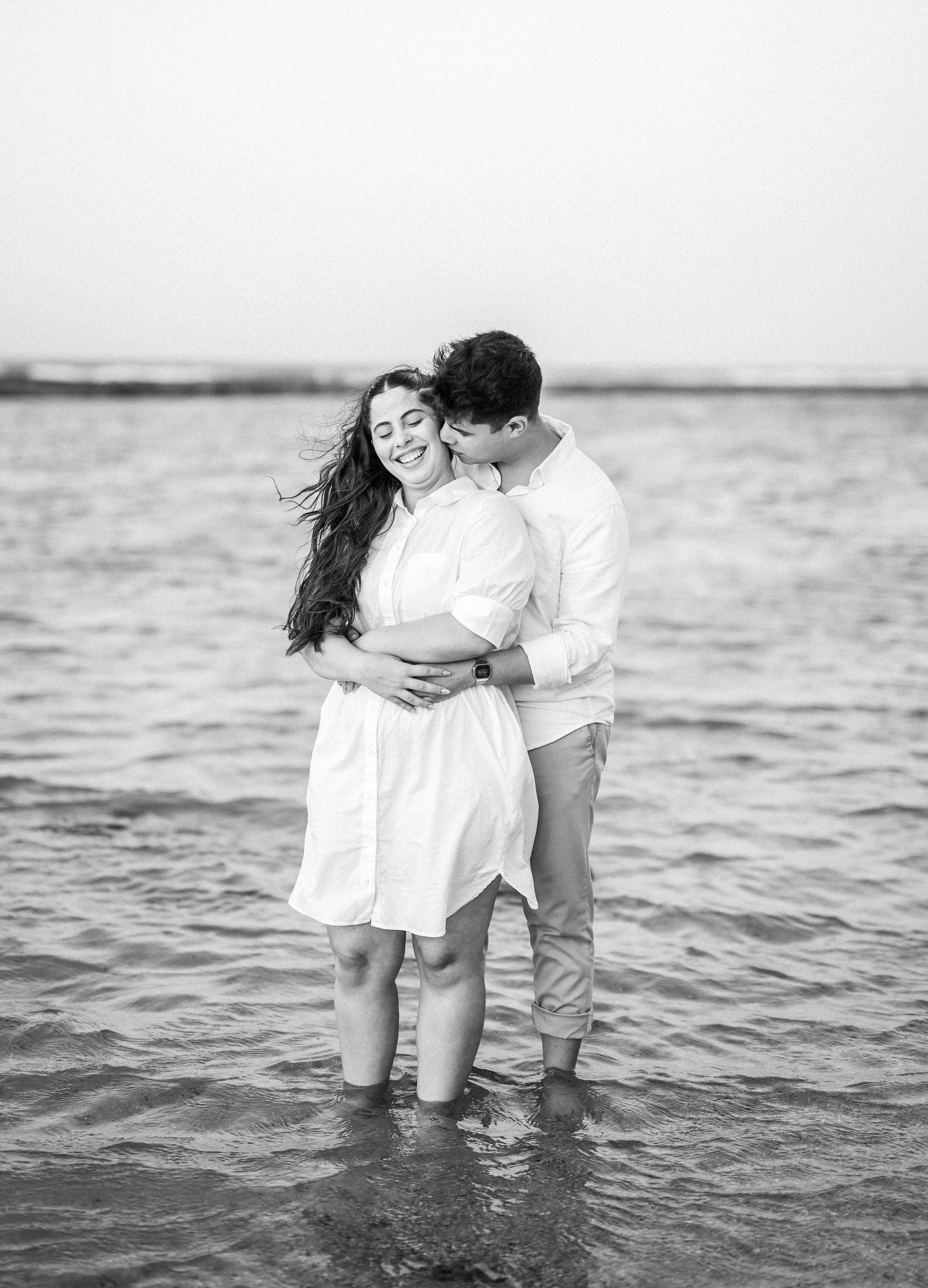 Romantic couple embracing in shallow ocean waters at sunset in black and white.