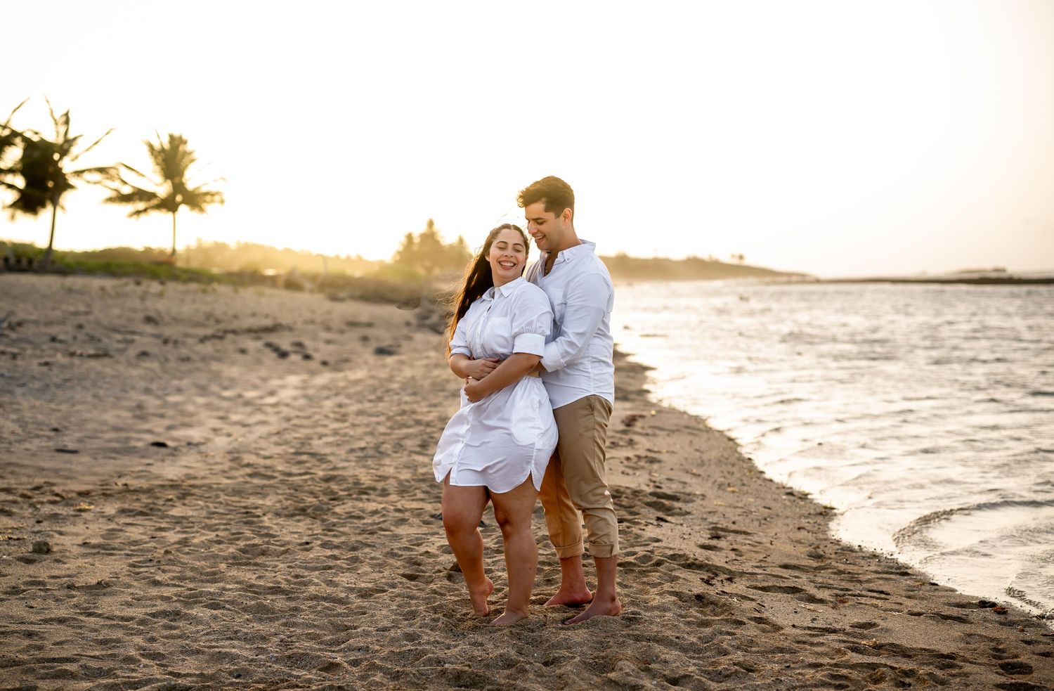 Couple in white clothes sharing tender moment on beach during sunset.