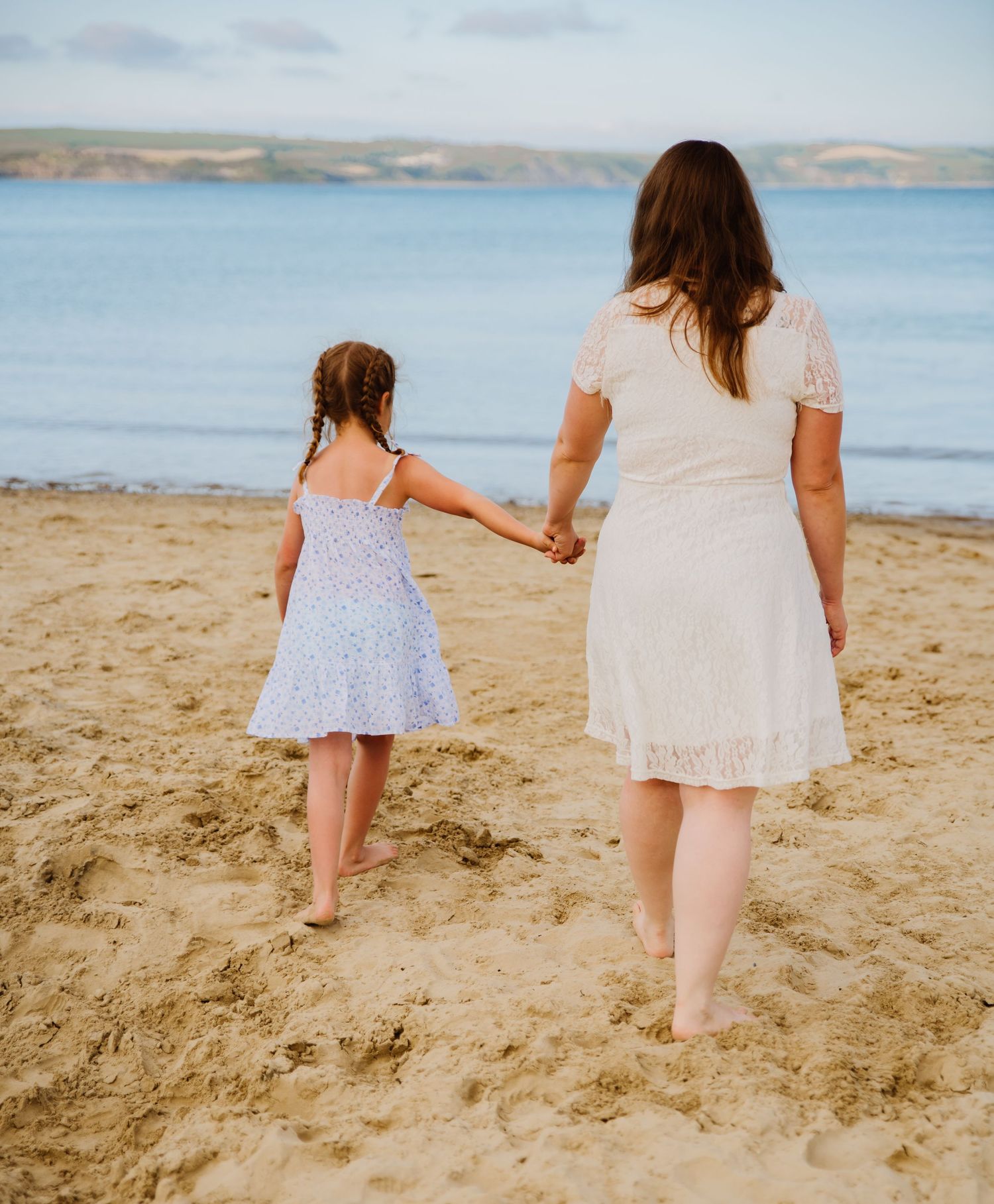 A mother and her daughter walk hand in hand on Weymouth Beach Dorset. They are walking towards the sea on the golden sandy beach