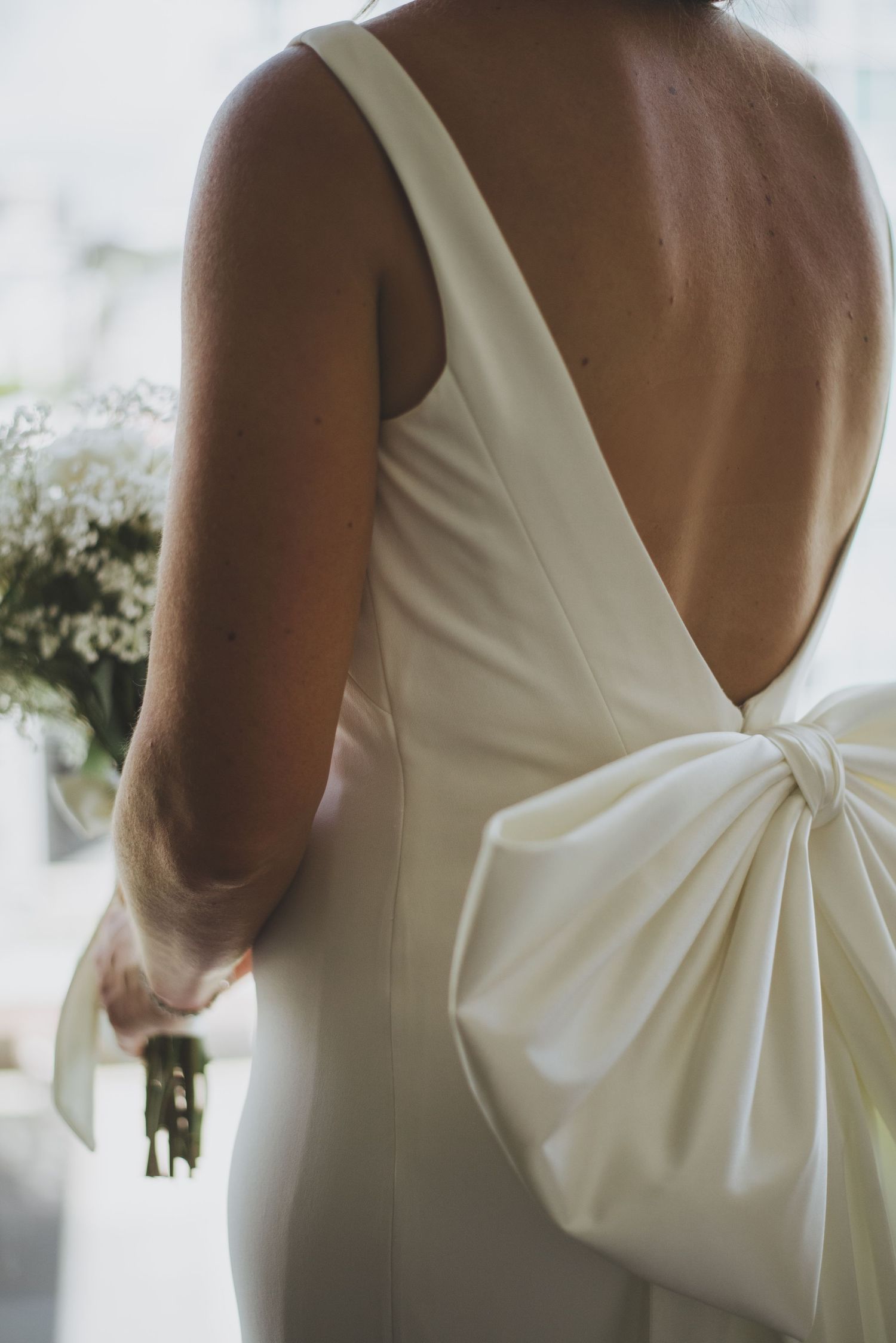 Elegant white wedding dress with dramatic bow detail and open back design.