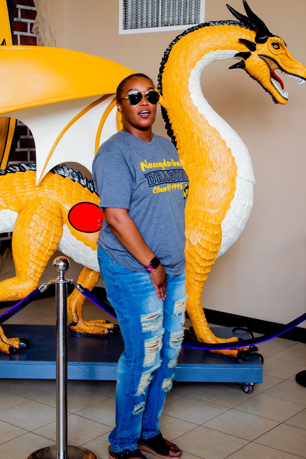 A large yellow and white dragon display statue stands next to someone wearing sunglasses, jeans and a gray t-shirt.