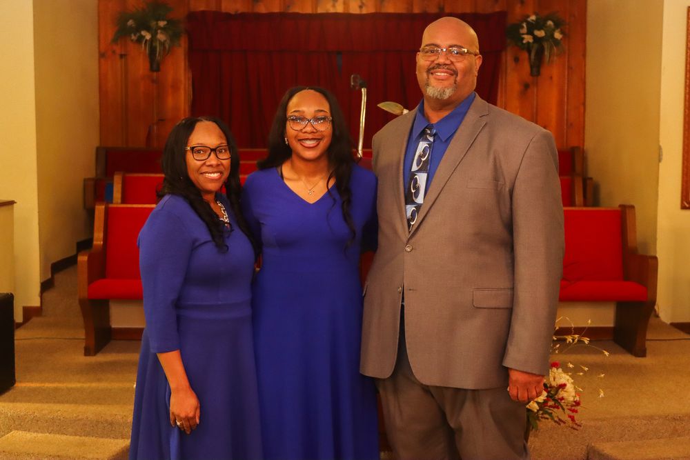 A group in blue and grey formal attire poses together in a church or event venue hallway.