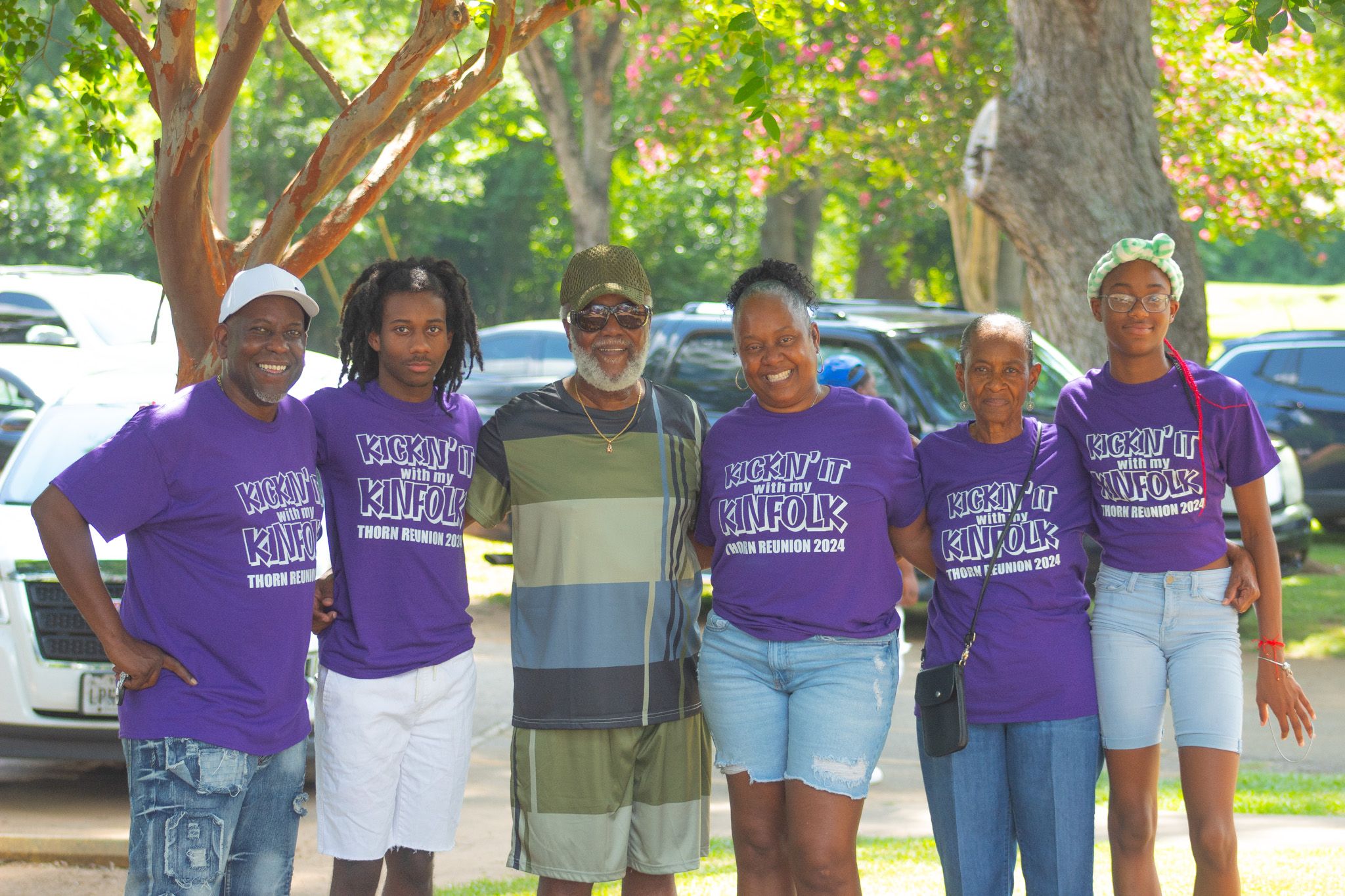 A group of people wearing matching purple and white t-shirts stand together outdoors in a casual gathering.