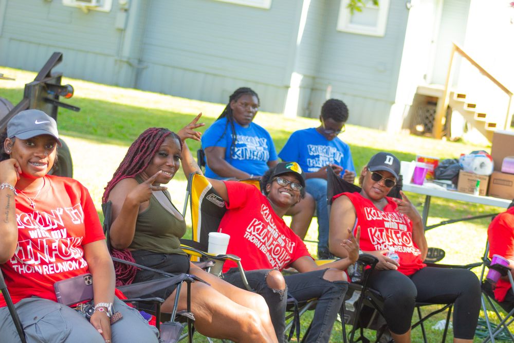 People in red shirts sit in folding chairs during an outdoor gathering event.