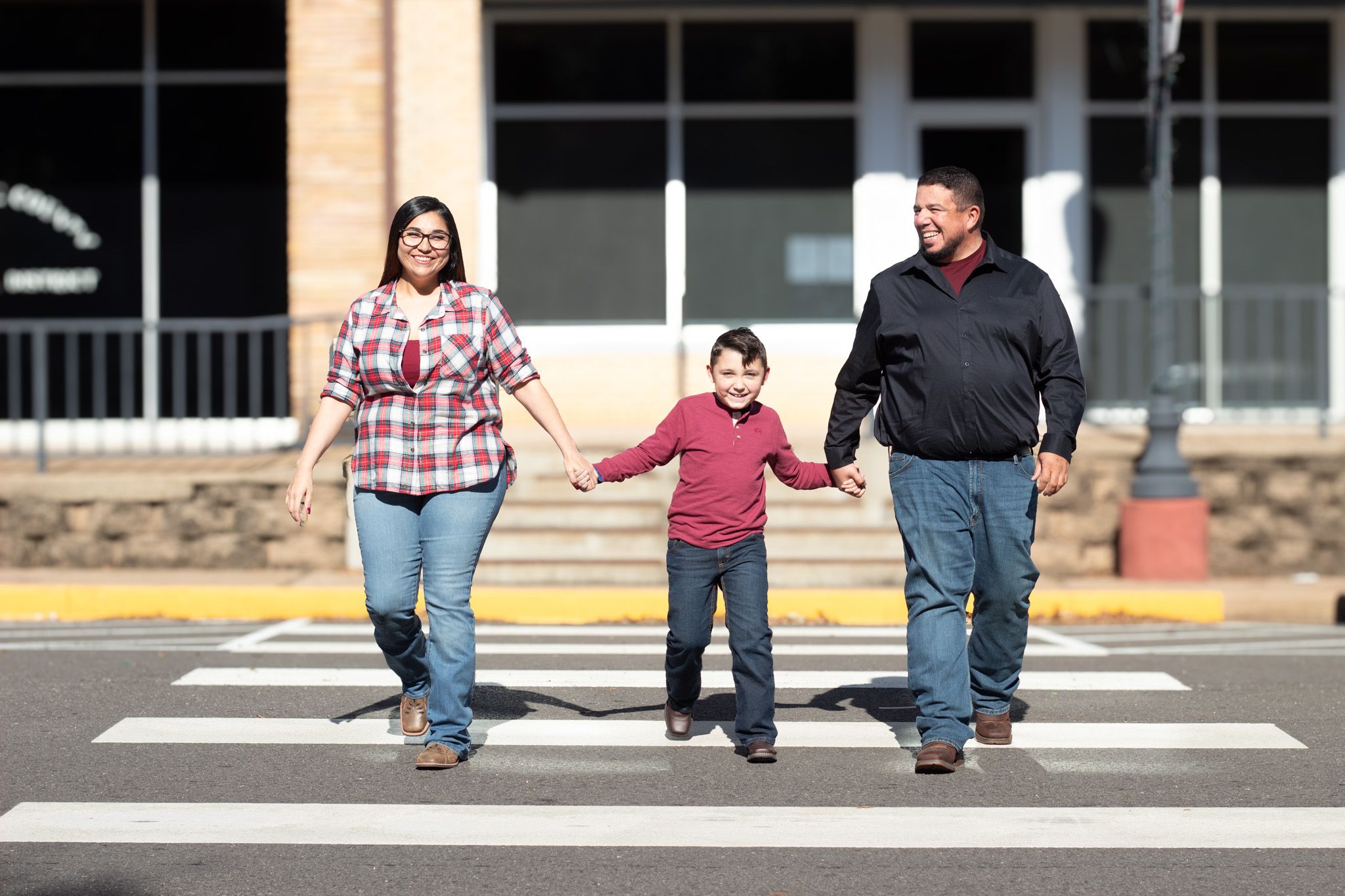 Three people holding hands while walking across a crosswalk in front of a building.