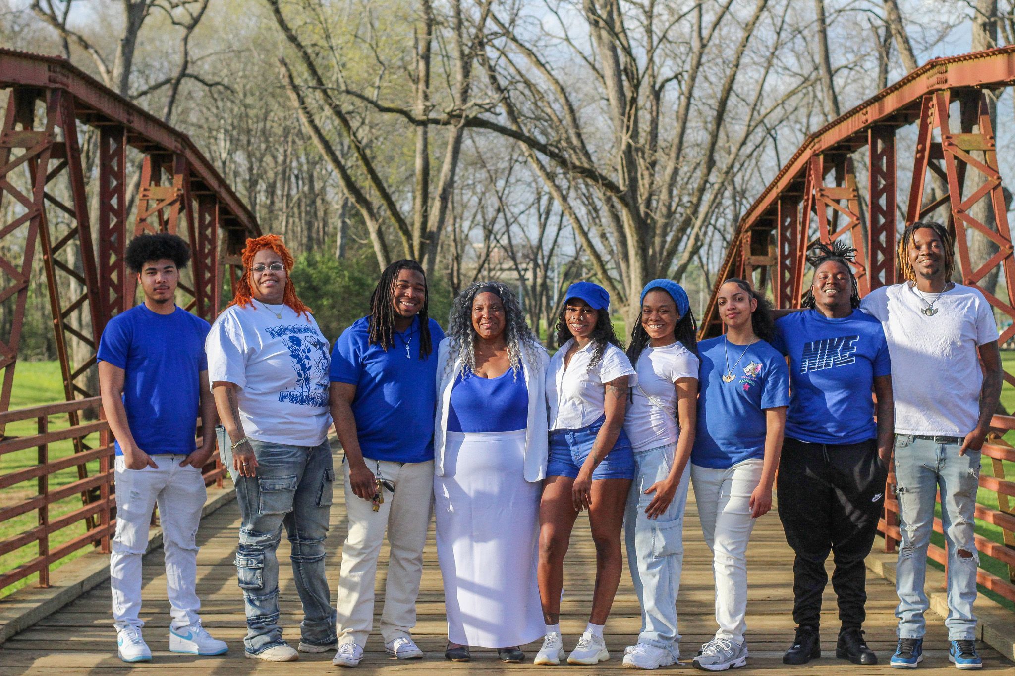 A group wearing matching blue and white outfits poses together outdoors in a park-like setting during a photo session.