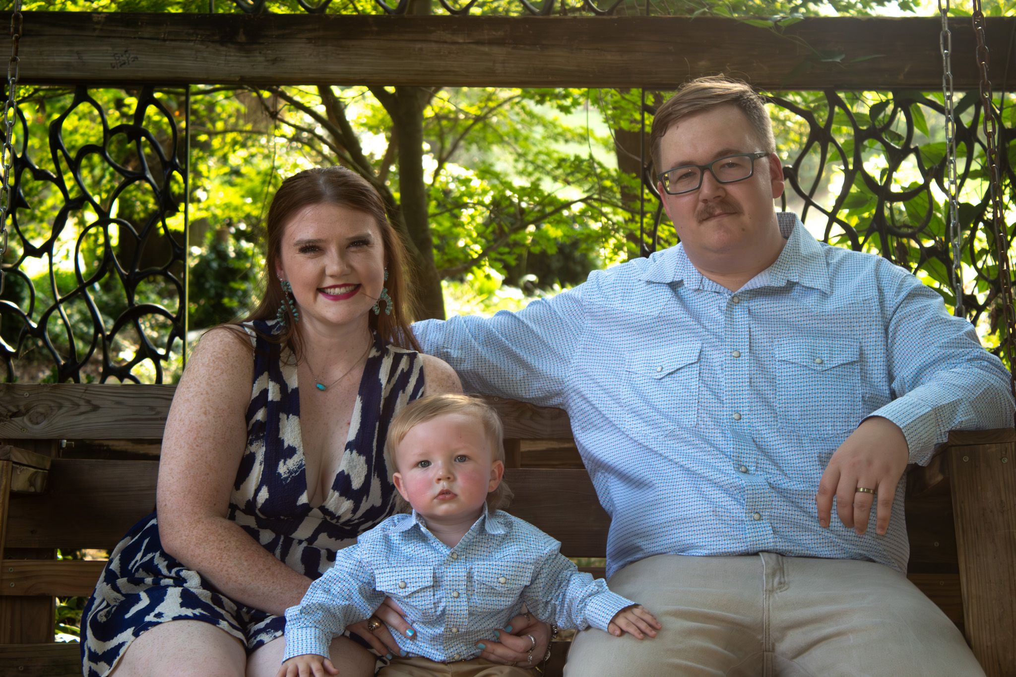 Family sitting together on wooden bench in lush garden setting on sunny summer day.