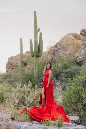 A flowing red dress contrasts dramatically against desert cacti and rocky terrain in a fashion photoshoot.
