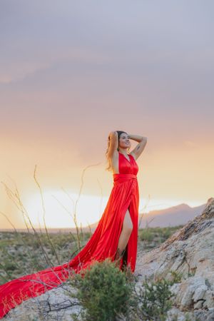 Elegant red dress flows in desert breeze during golden hour photoshoot with mountain backdrop.