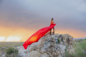 Dramatic red fabric catches wind against desert sunset sky and rocky terrain.