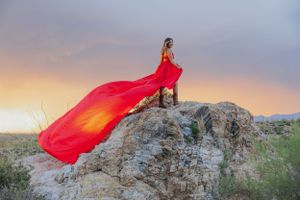 Flowing red fabric creates movement against rocky desert landscape at dusk.