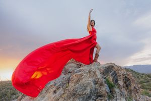Windswept red dress creates dynamic shapes against cloudy desert sky.