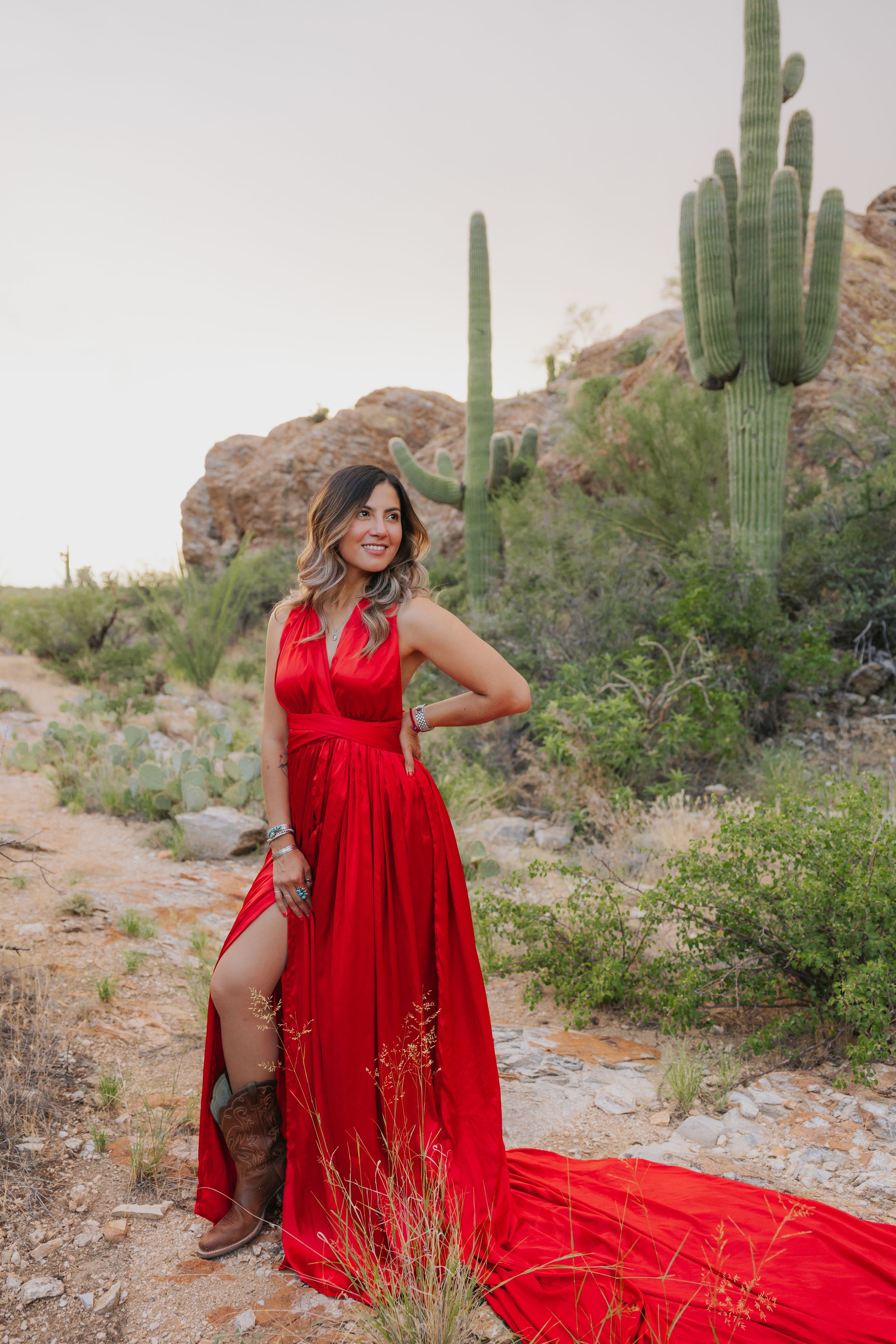A dramatic red dress trails across desert terrain surrounded by saguaro cacti and desert flora.