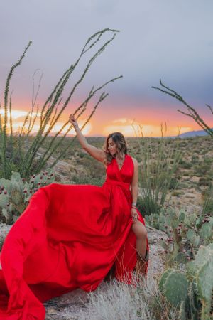 Red dress flows elegantly among desert cacti and brush during golden hour in the wilderness.