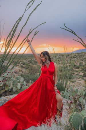 Dramatic red gown contrasts against desert plants and mountains during a vibrant sunset photoshoot.
