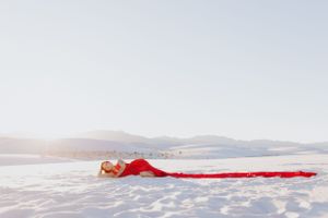 Flowing red fabric creates a striking line across pure white sand with distant mountains.