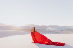 Red dress creates dramatic contrast against white sand dunes in a minimalist desert landscape.