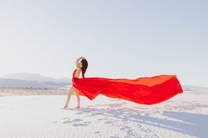 Bright red fabric flows gracefully across pure white sand dunes under a clear blue sky.