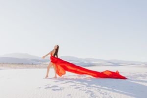 Long red fabric creates sweeping lines across pristine white sand with mountains in the distance.