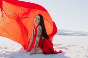 Vibrant orange-red fabric dances in the wind against stark white sand dunes.