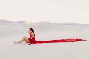Long red fabric stretches across pristine white sand creating an artistic composition.