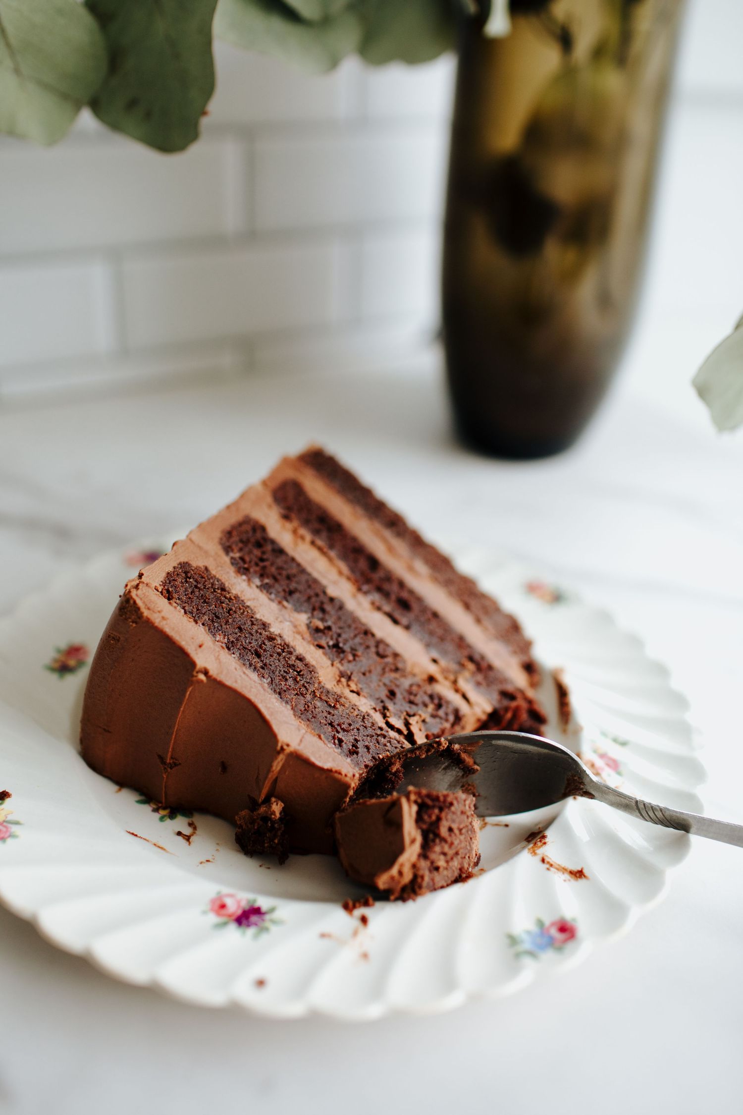 Slice of layered chocolate cake with mocha frosting on a vintage floral plate.