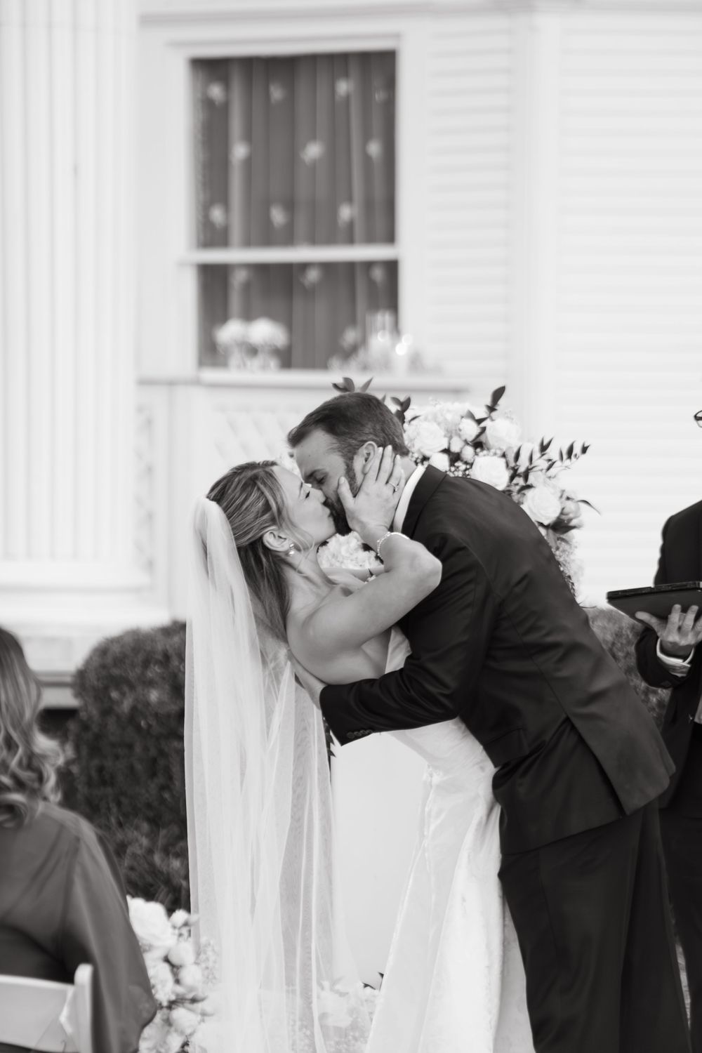 Romantic wedding kiss captured in black and white against a white columned building.