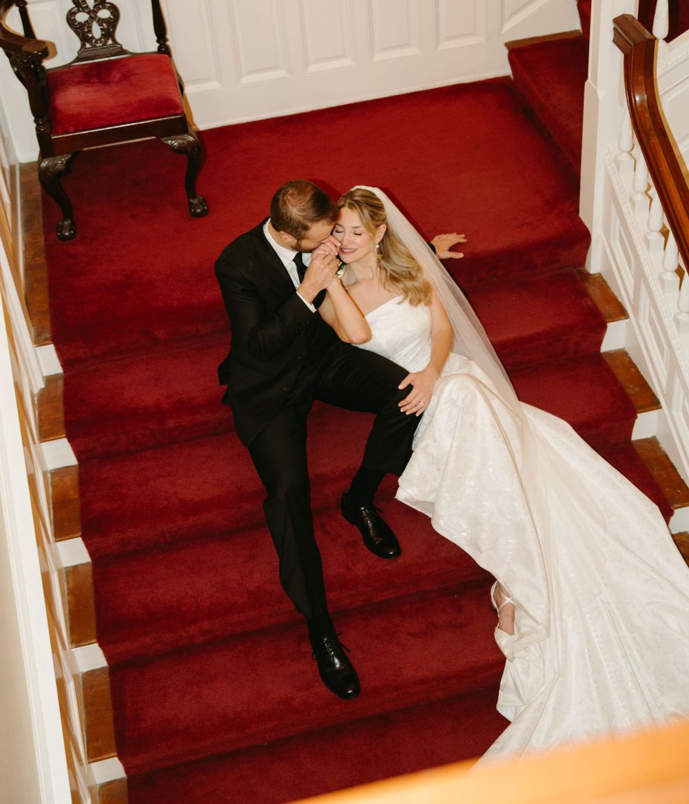 Couple descending red-carpeted stairs in an elegant white interior.