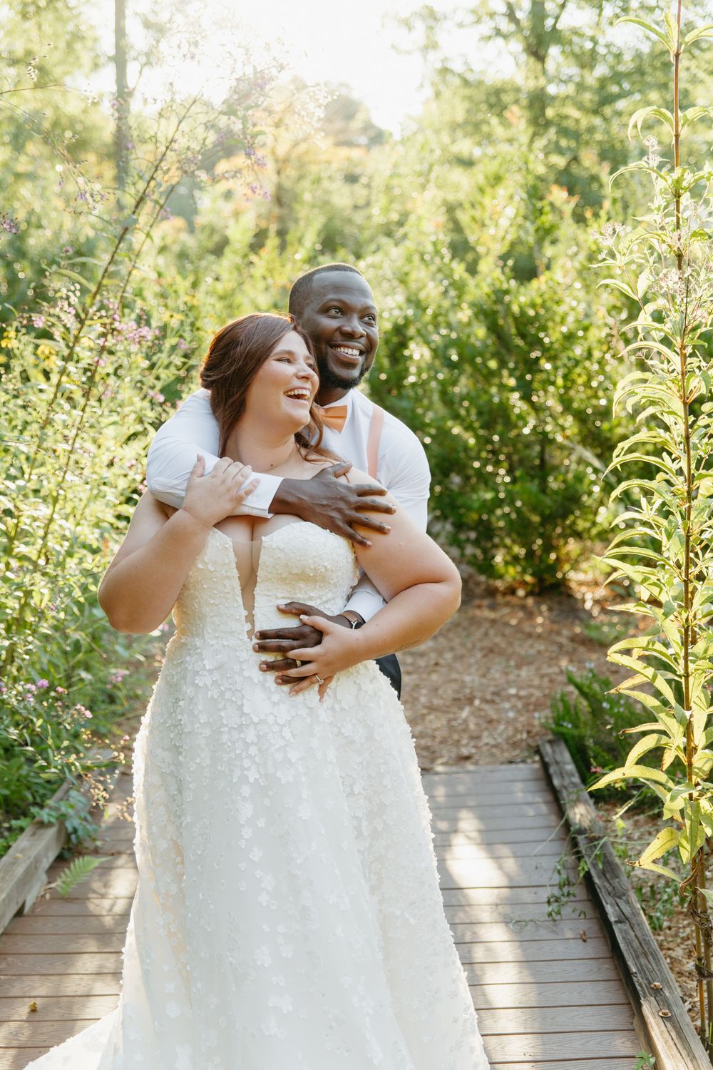 Newlyweds share joyful moment together on wooden pathway in garden setting.