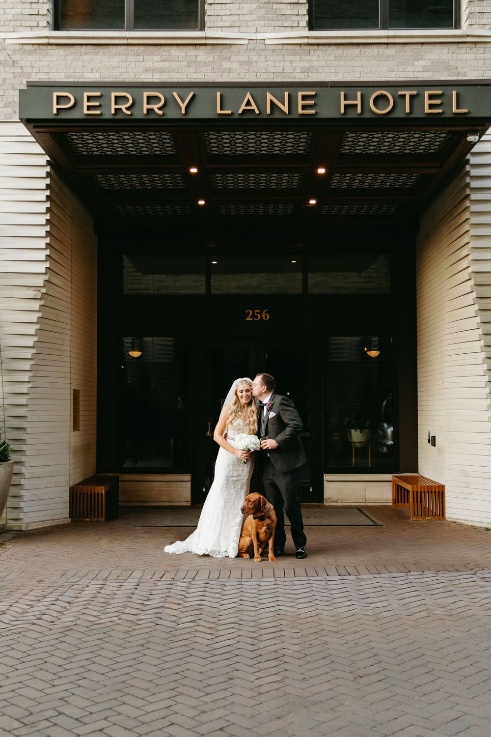 Wedding couple poses outside Perry Lane Hotel entrance with white brick facade.