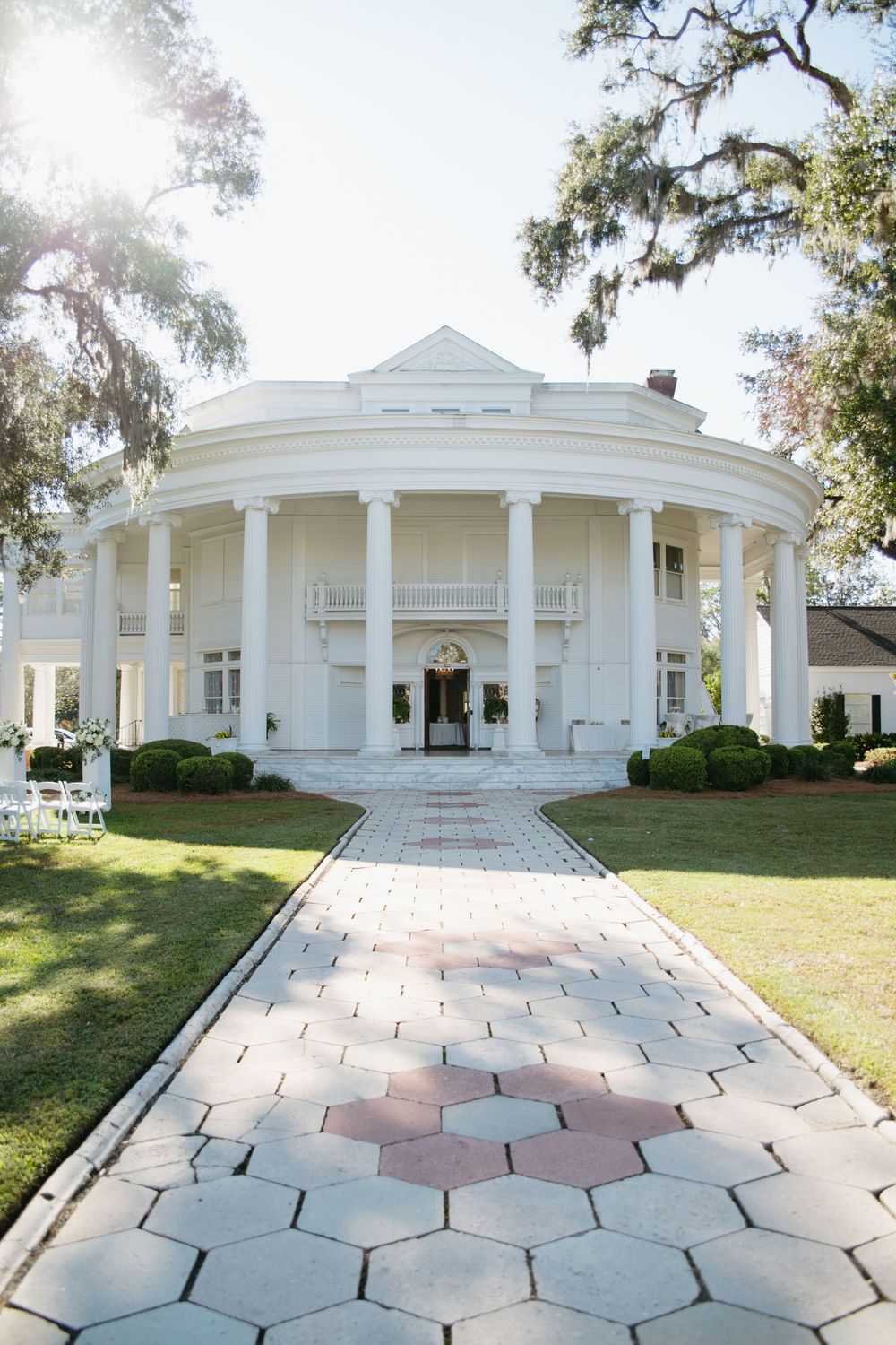 Elegant white colonial style mansion with hexagonal paved courtyard.