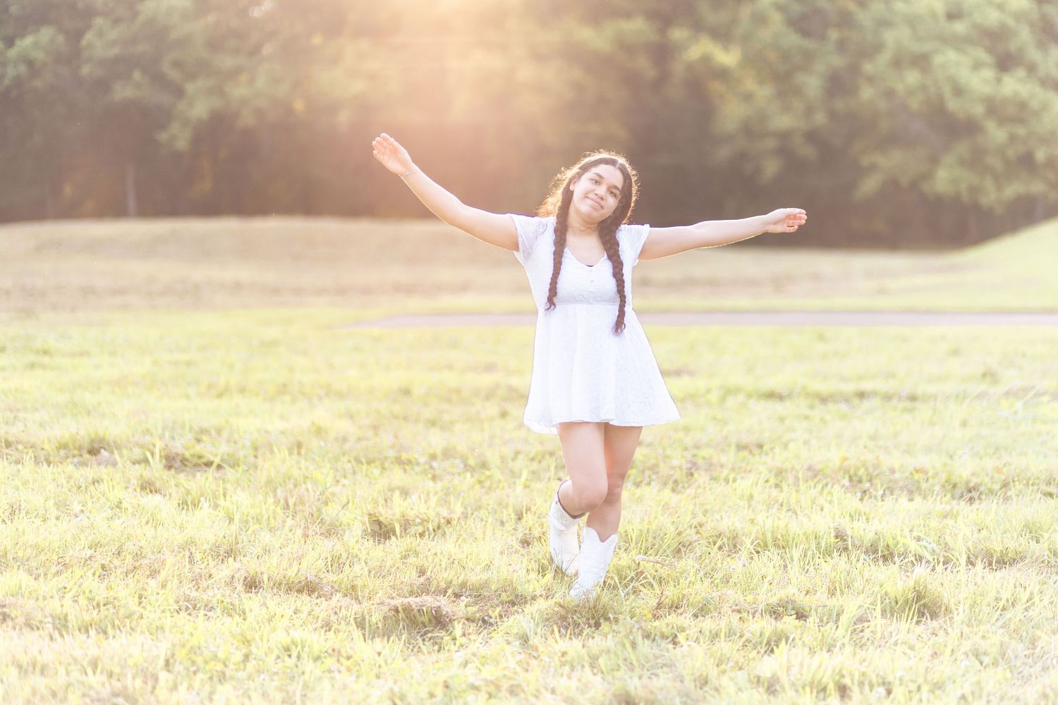 High school senior in field with arms up.